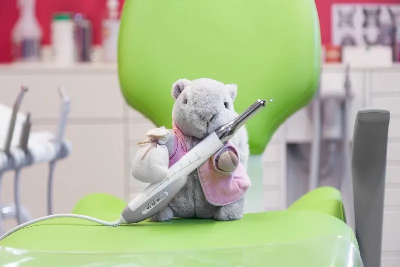 Peluche mascotte avec caméra intra-orale sur un fauteuil pédiatrique vert — Cabinet 21 Libération